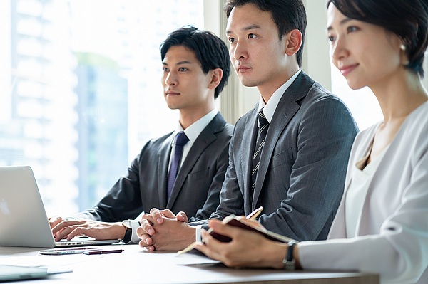 会議室で真剣に話を聞く若いビジネスパーソン